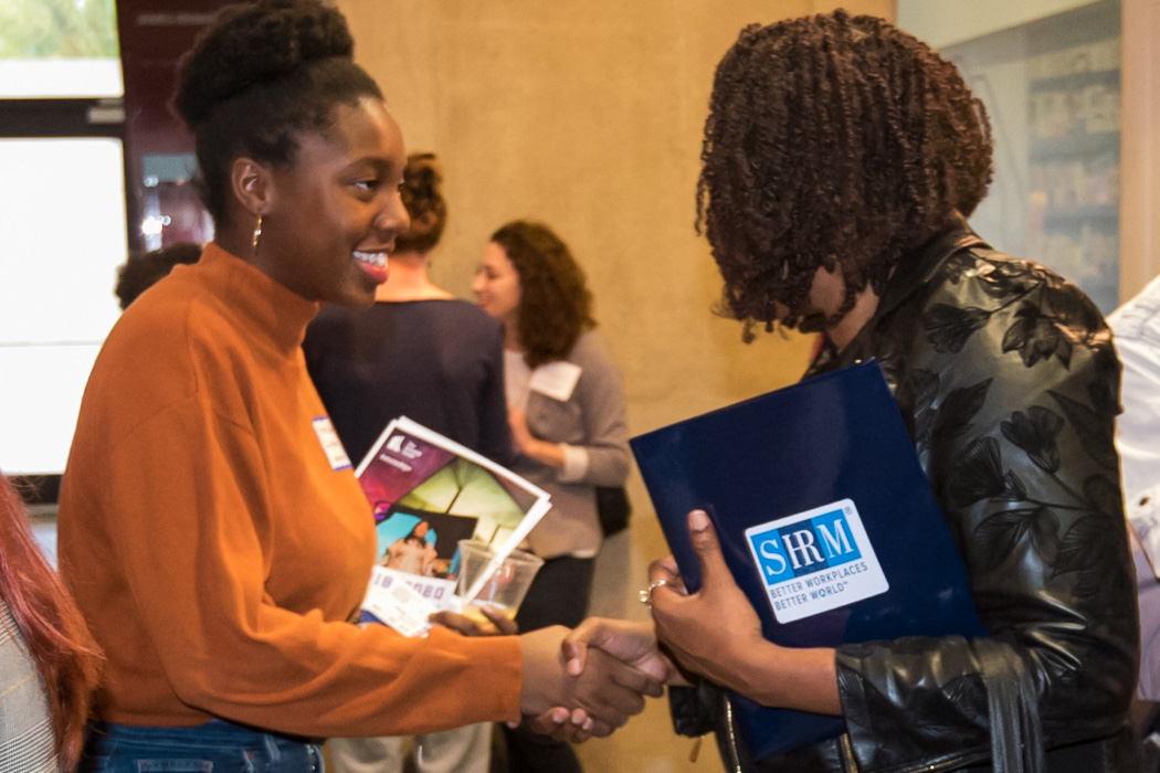 A student and alumni attendee shake hands at a networking event