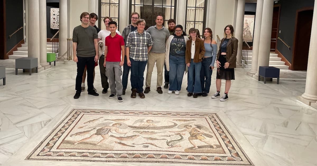 Dr Fedyashin and student tour group in front of Roman mosaic in the floor.