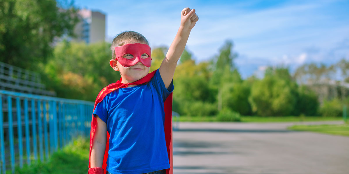 Kid dressed as a superhero raises one fist to the sky