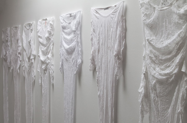 Seven delicate shrunken t-shirts are pinned to the wall