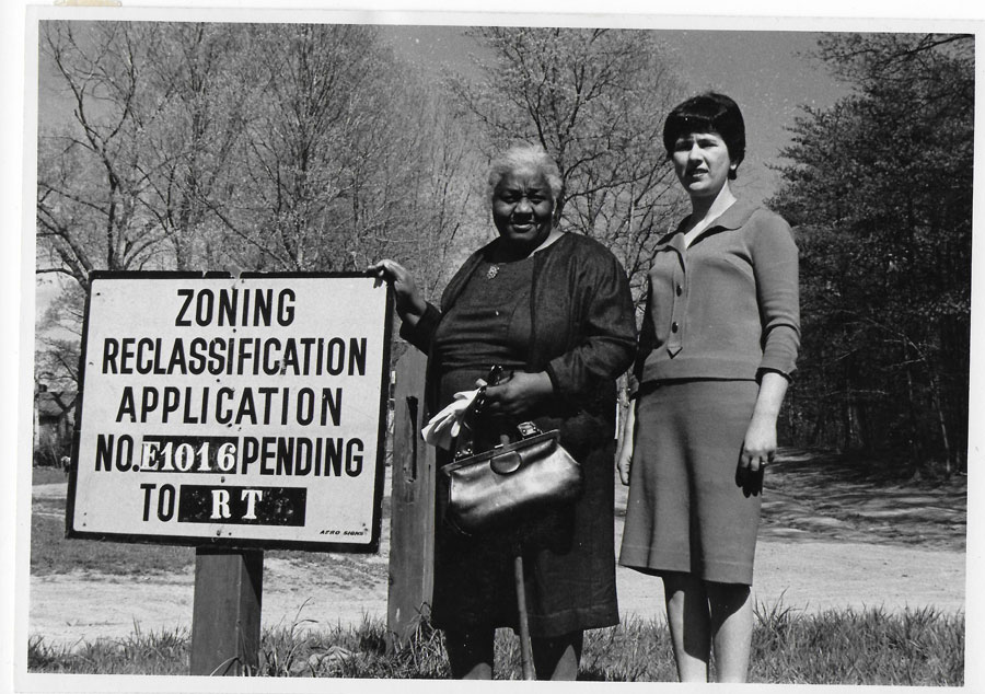 Two women and a sign saying 'Zoning Reclassfication Application NO. E106 Pending'