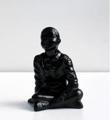 Glossy black sculpture of boy sitting on floor with legs crossed