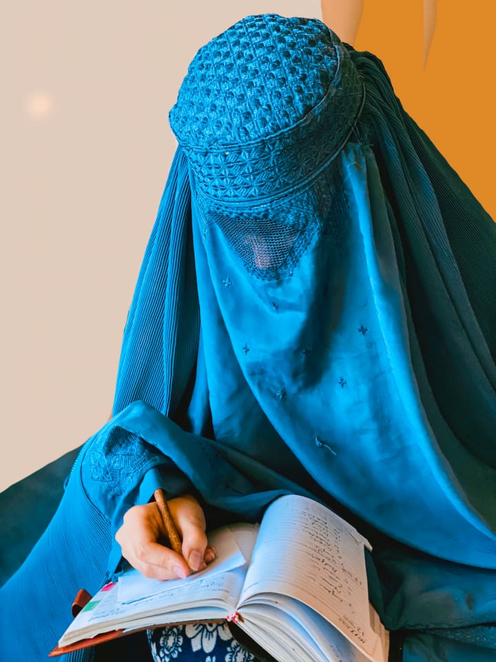Person in blue veil writing in a hardbound journal.