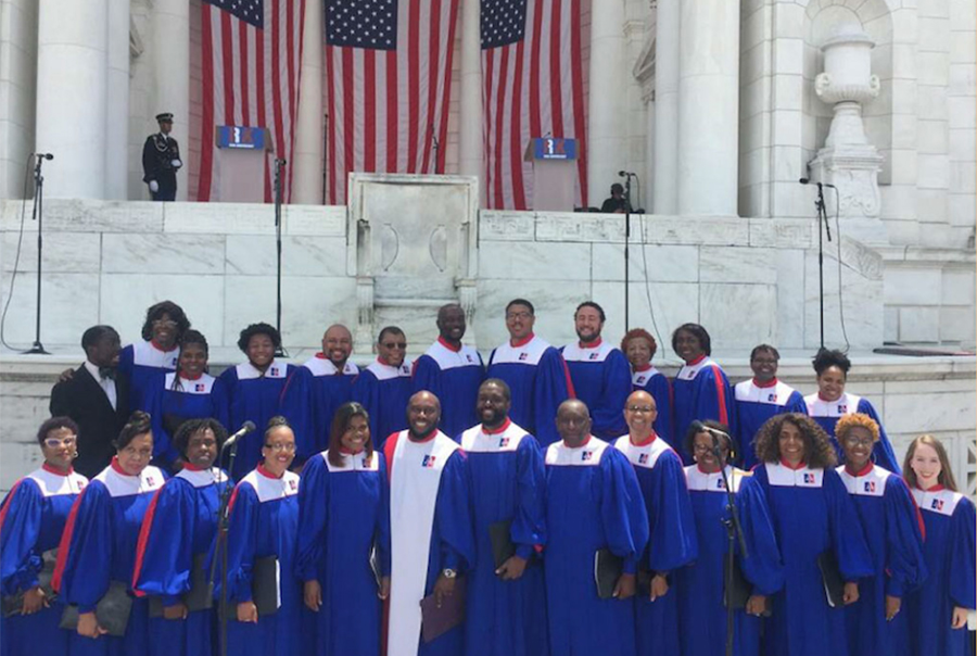 Choir in robes stands in front of marble building with American flags