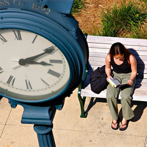 Student reading under clock on AU campus quad.