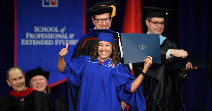 A student in cap and gown holds a diploma