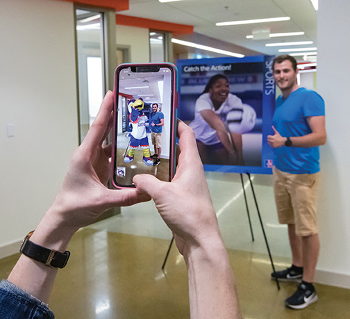 A prospective student poses with an augmented reality Clawed mascot
