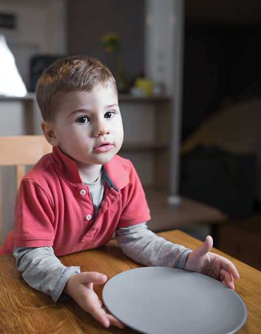 Child sits at a table with an empty plate