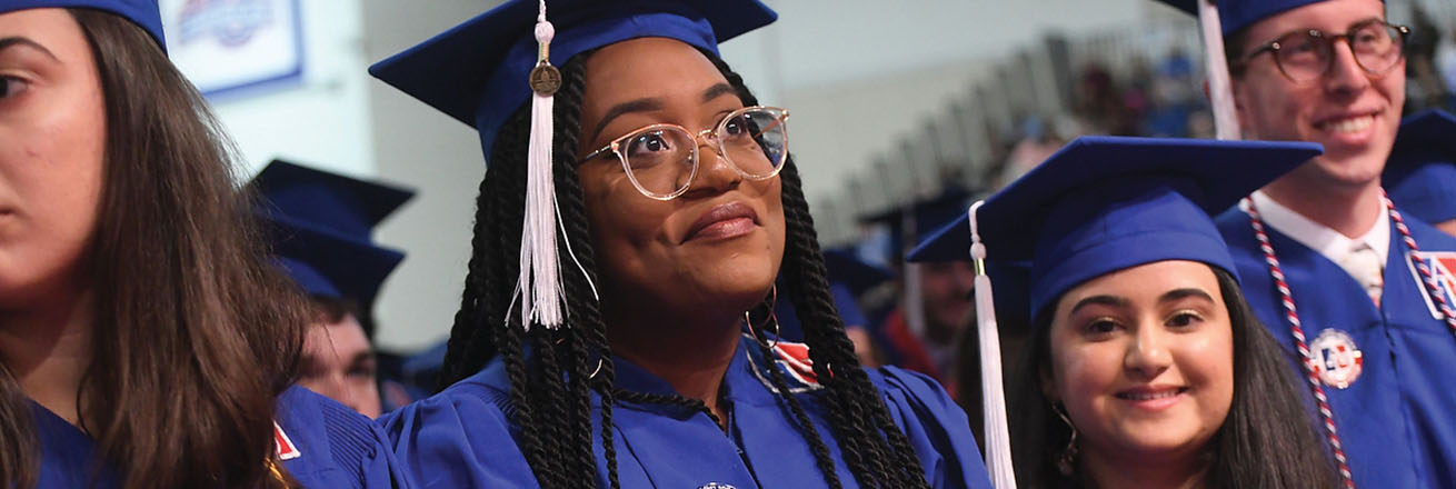 Four graduates stand in cap and gown at commencement