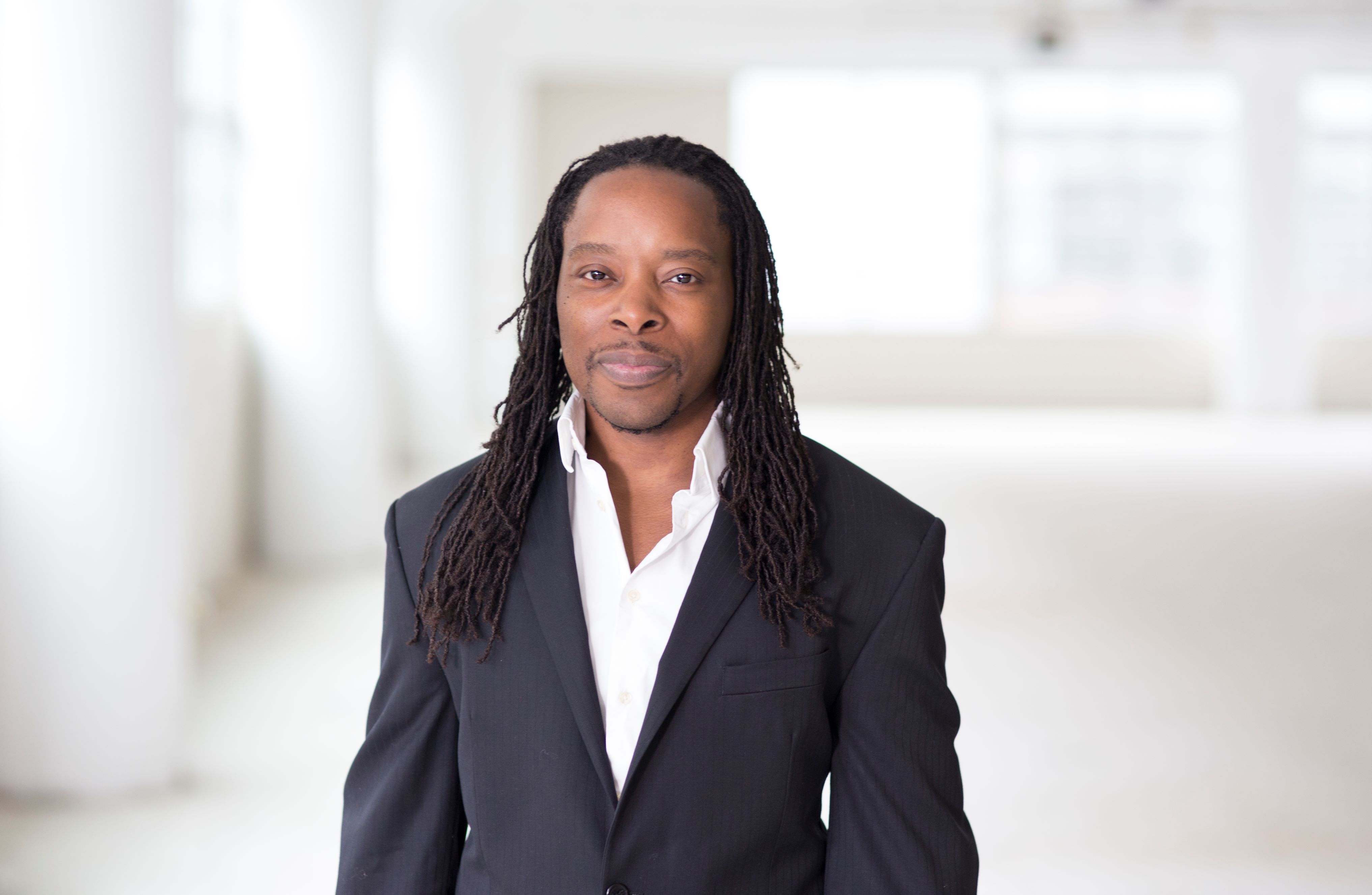 Dr. Omekongo Dibinga, a person with dark skin and black hair posing professionally wearing a dark suit.