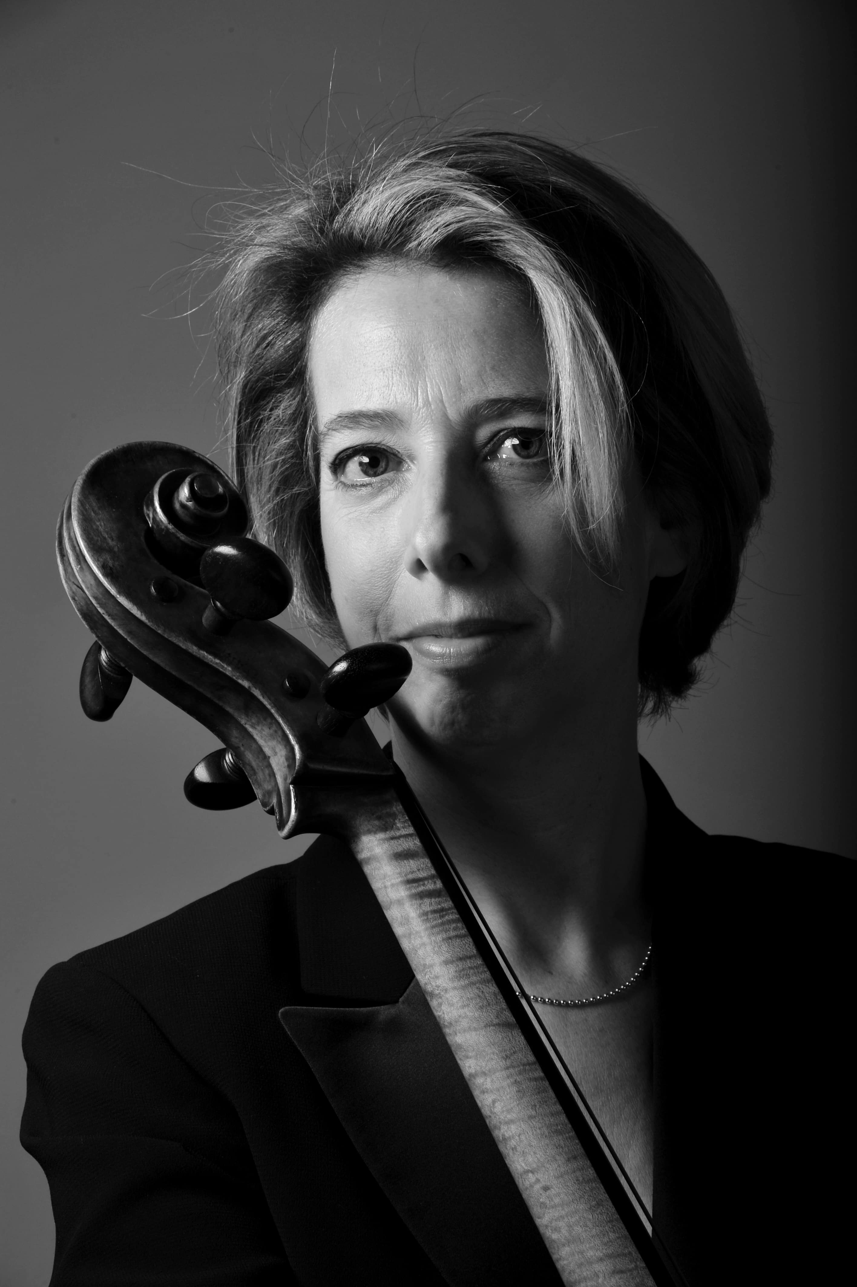 Black and white headshotof Prof Sider wearing a black blazer and holding her cello
