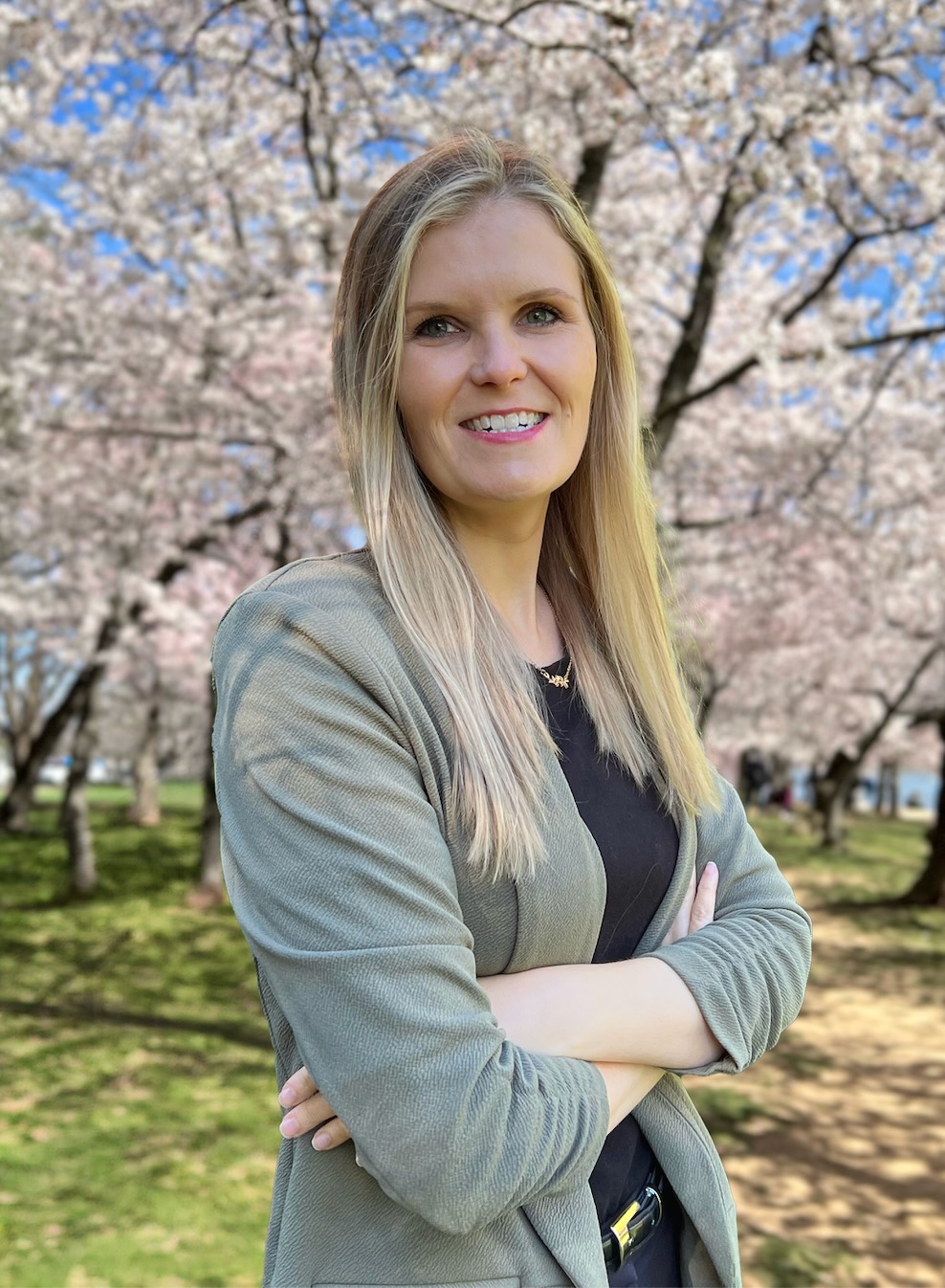Professor Wilson-McDonald, a light-skinned woman with blonde hair, poses in front of cherry blossom trees in bloom.