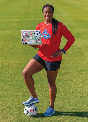 Marsha Harper holds a laptop and stands on top of a soccer ball