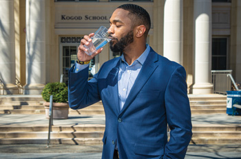 Korey Salter drinks from a water glass in front of the Kogod School of Business