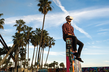 Matthias McCoy-Thompson wears a VR headset while sitting on a graffitied wall at Venice Beach