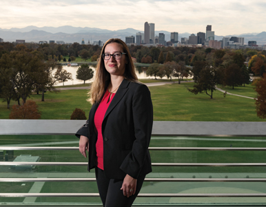 Christine Hernandez stands on a balcony with downtown Denver in the background