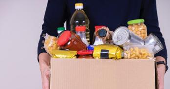 person holding box filled with produce and canned goods