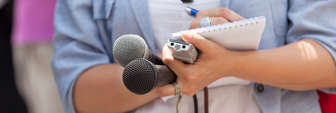 Female journalist holding microphones, recorder and notepad and pen