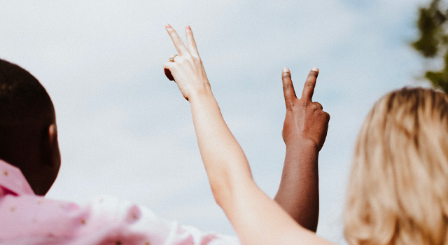 a white girl and a black mans hands cross while holding up the peace sign with their fingers