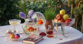 A Nowruz table is set with apples, sprouts, garlic, candles, spices, books, and goldfish