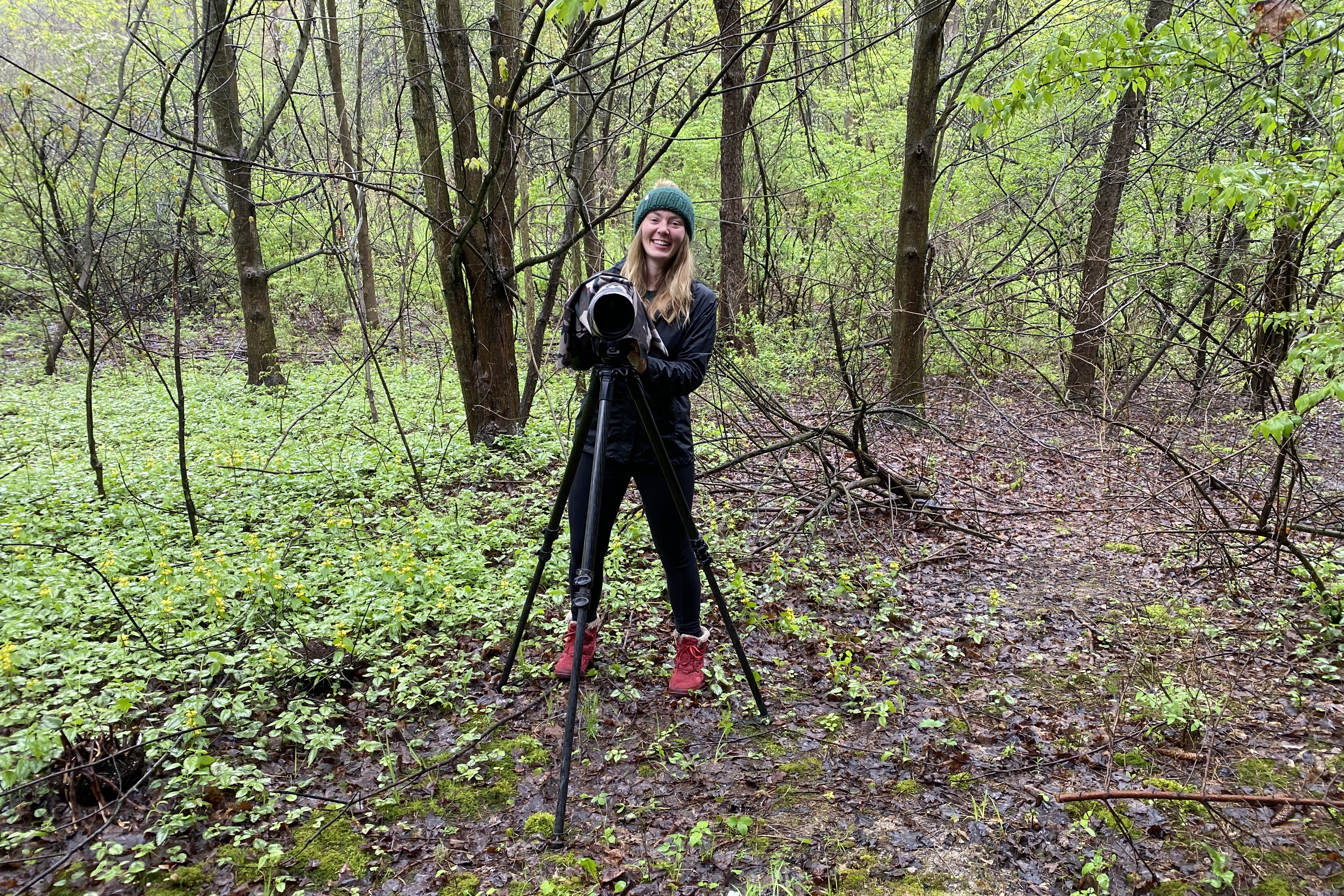Female student stands in forest with camera