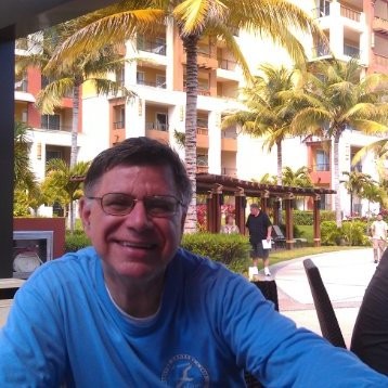 Man with glasses in front of beach hotel with palm trees