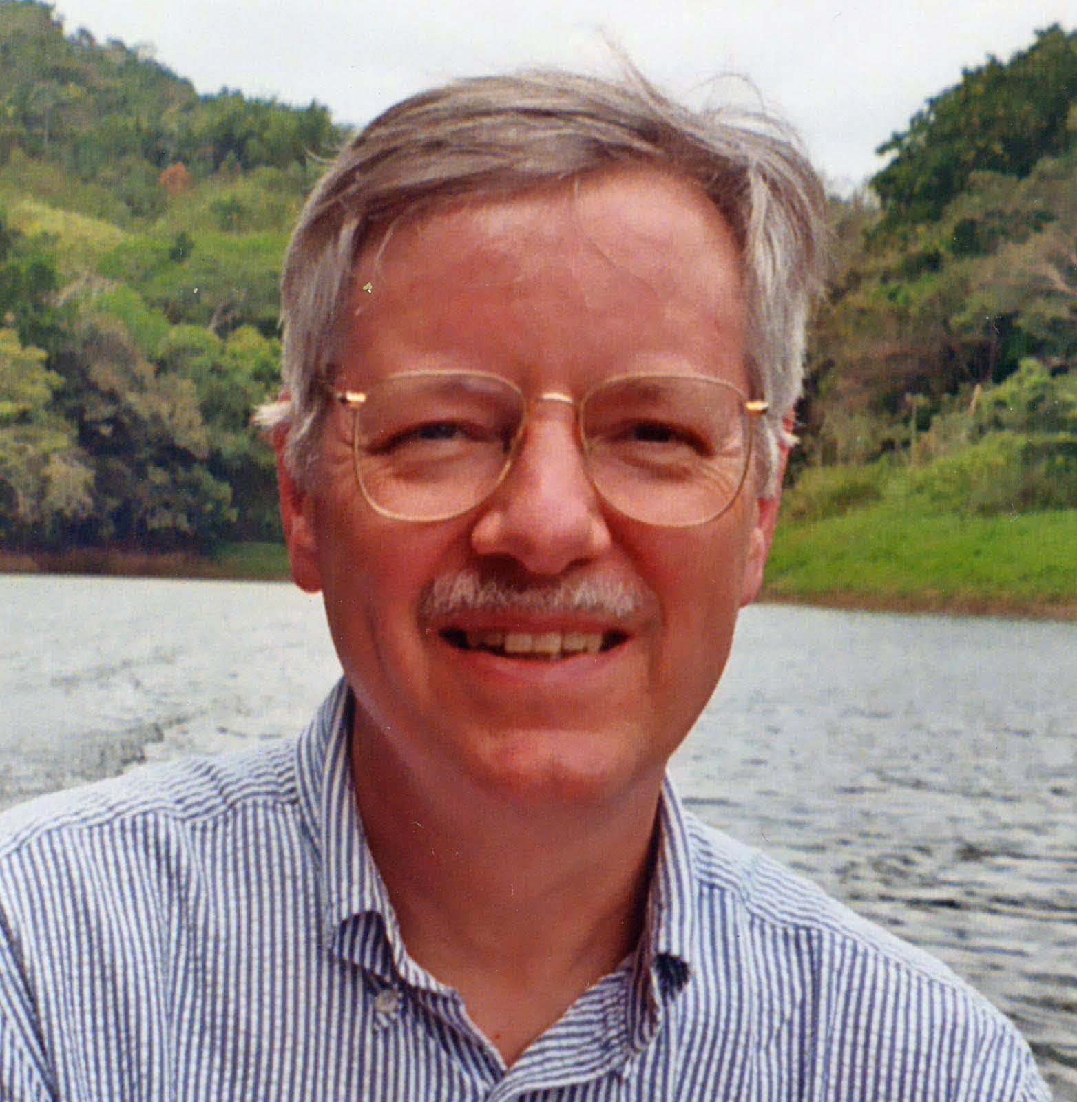 Man with mustache and glasses in front of a river