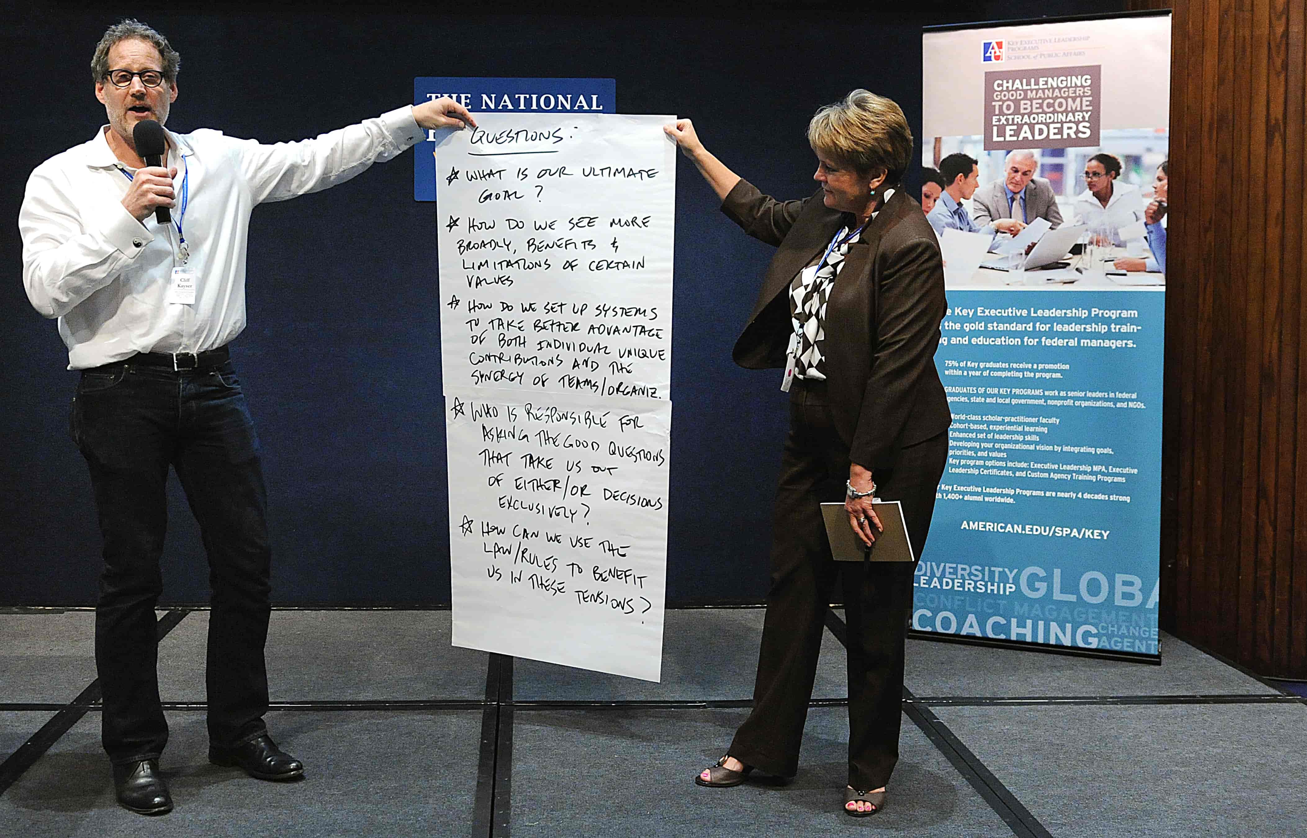 Two people hold a piece of paper that lists questions that will be answered during the conference.