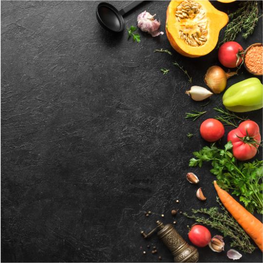 Black background with an assortment of vegetables and a spoon spanning the right side of the image