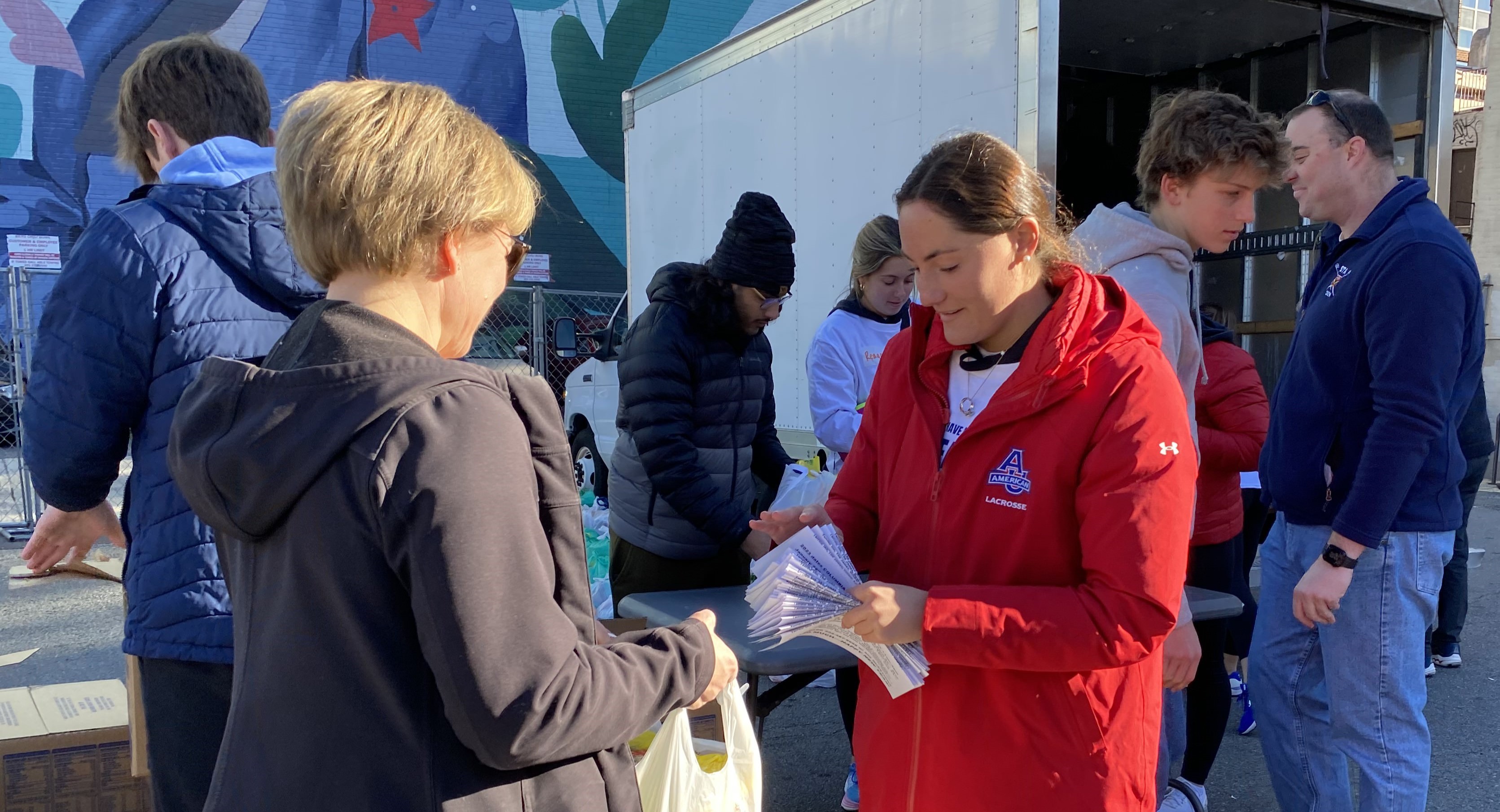 20230116_191014214_iOS - Copy AU student in red coat hands out food to community member.
