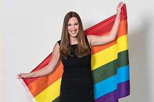 A photo of American University alumna Sarah McBride smiling in front of an LGBT rainbow flag.