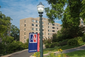 Light and pole with the AU flag, in between trees and in front of residence hall. 