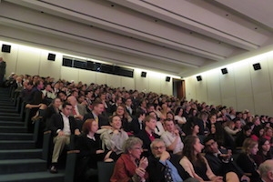 A crowd waits in their seats to watch a film.