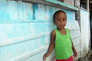Young Brazilian child standing against a blue wall.