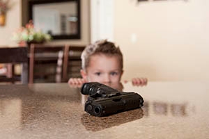 A small child staring at a hand gun within reach on a table.