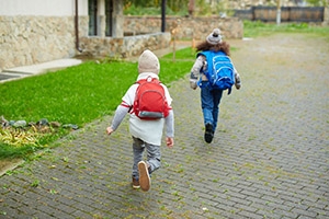 Two elementary school children walking on gray cobblestone street.