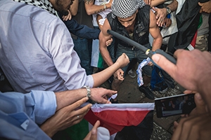 Close-up of a pro-Palestinian group gathering around a man lighting a match while being recorded on a smart phone.