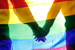 Two hands holding with gay pride flag overlaid.