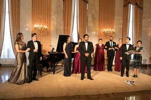 Ten young people in formal wear stand in front of a piano