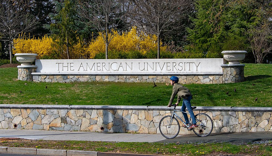 Student rides bike in front of Glover Gate