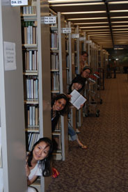 Students peaking out from behind library stacks.