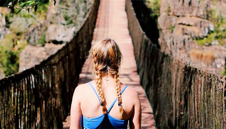 Student on thatched bridge crossing natural gorge.