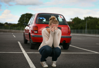 A young girl crys behind a car in a parking lot.