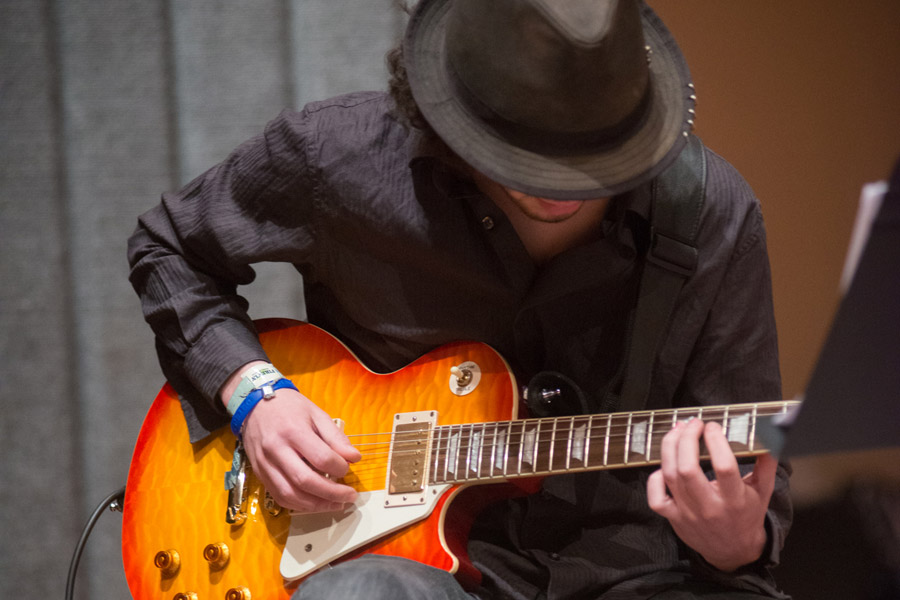 Person in hat leans over guitar to play