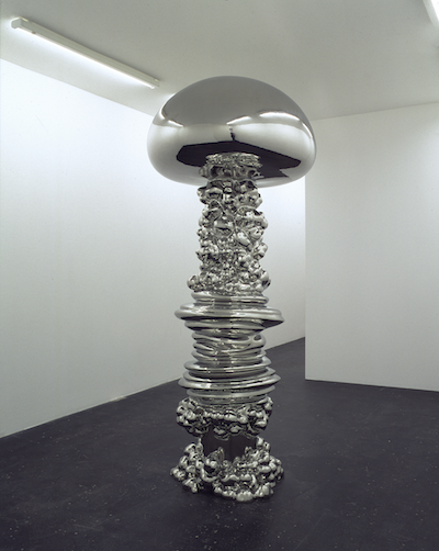 A large silver sculpture. Stacked on the bottom with a mushroom like top.