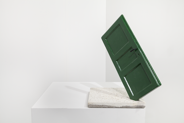 A green door is stuck in a white granite block.