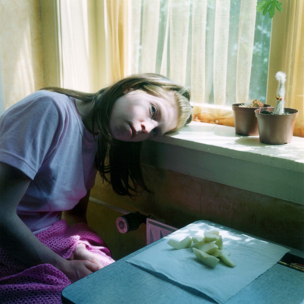A young woman in an interior, leaning her head on a windowsill looking at the camera
