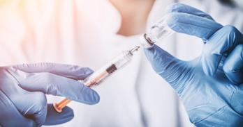 Gloved hands holding vial and syringe