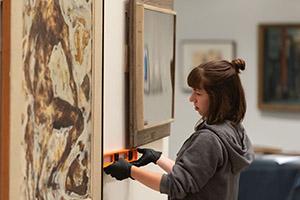 A woman uses a level to measure adjust a painting on the wall