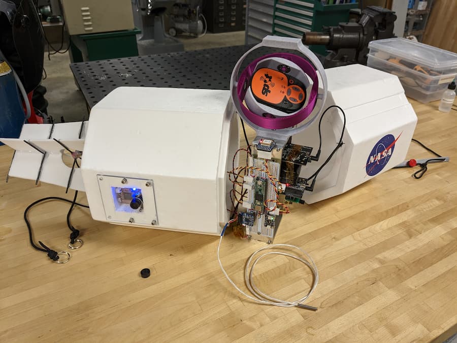 The balloon payload, prior to final assembly.  (Left to right: transmitting antenna, camera for live photos (blue light), flight computer & detector assembly, SPOT GPS for recovery (orange), thermometer (gray cable out front)